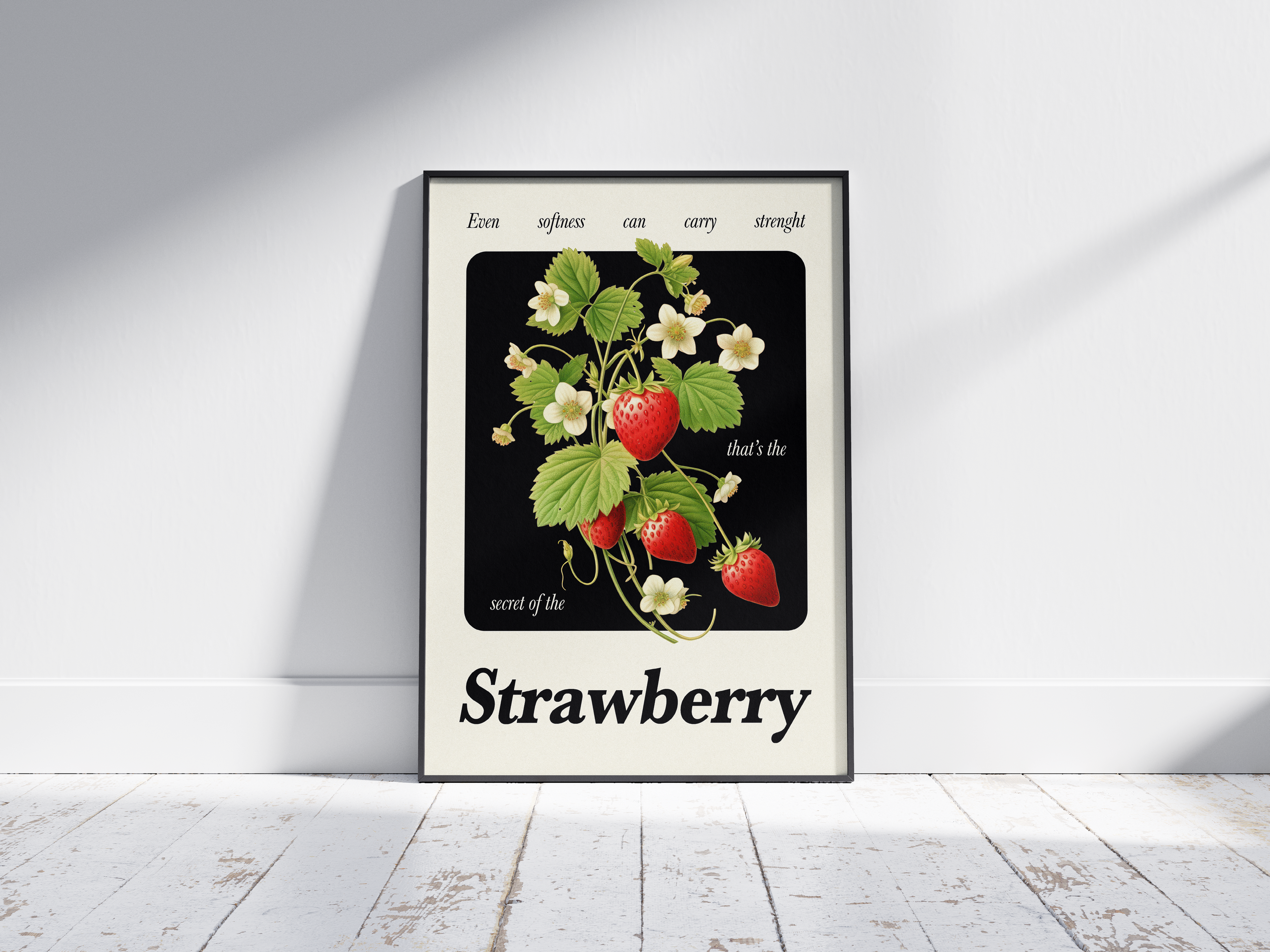 Poster in black frame with illustration of a strawberry plant, red fruits, white blossoms, green leaves. Text: "Even softness can carry strength" and "that's the secret of the Strawberry". Against a white wall on a wooden floor.