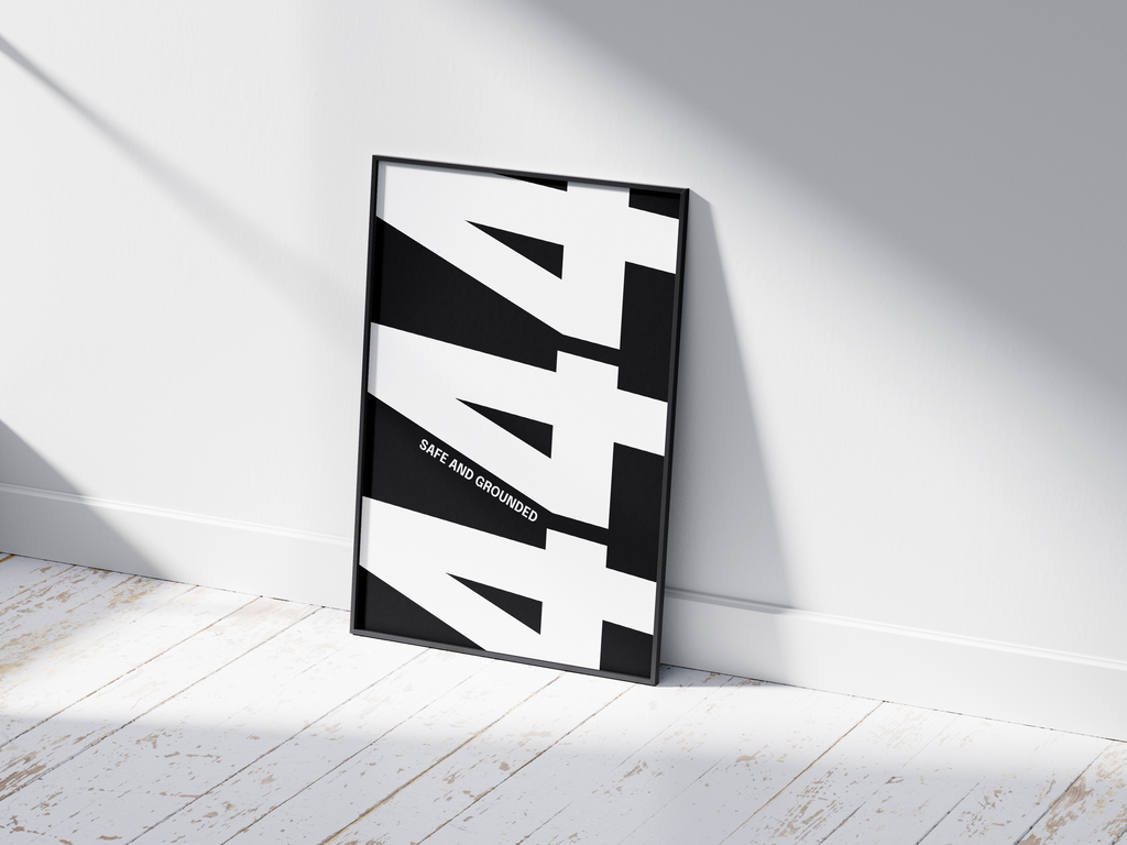 Minimalist black and white abstract poster featuring the repeated number 444 design and the quote "Safe and grounded," framed and leaning against a white wall. Inspiring modern wall art for a secure, contemporary home or office interior.