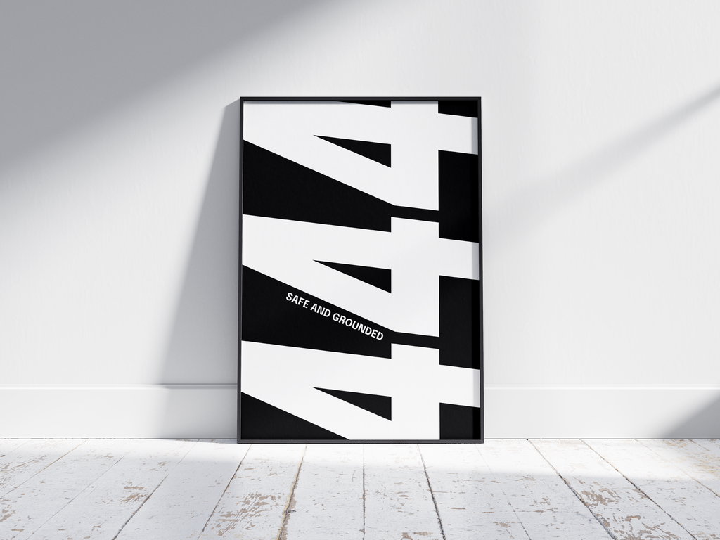 Minimalist black and white abstract poster featuring the repeated number 444 design and the quote "Safe and grounded," framed and leaning against a white wall. Inspiring modern wall art for a secure, contemporary home or office interior.