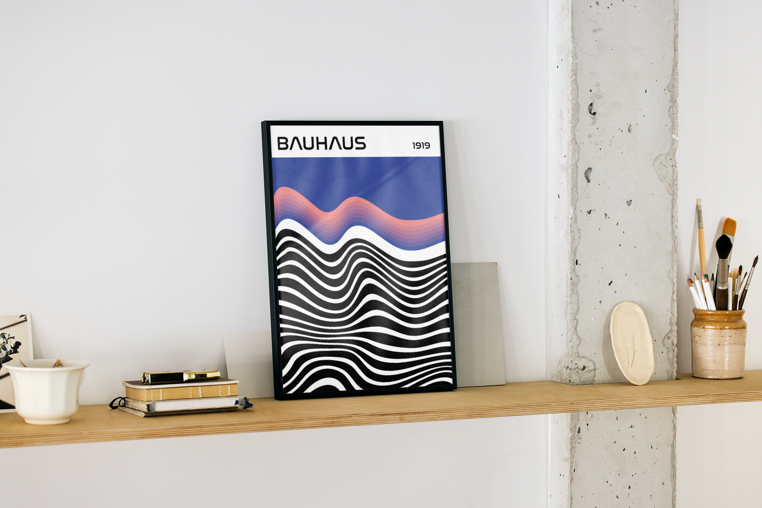 A framed modern poster with the word "BAUHAUS" and an abstract design of wavy lines in blue, pink, and black, displayed on a wooden shelf in an artist's workspace or gallery room.