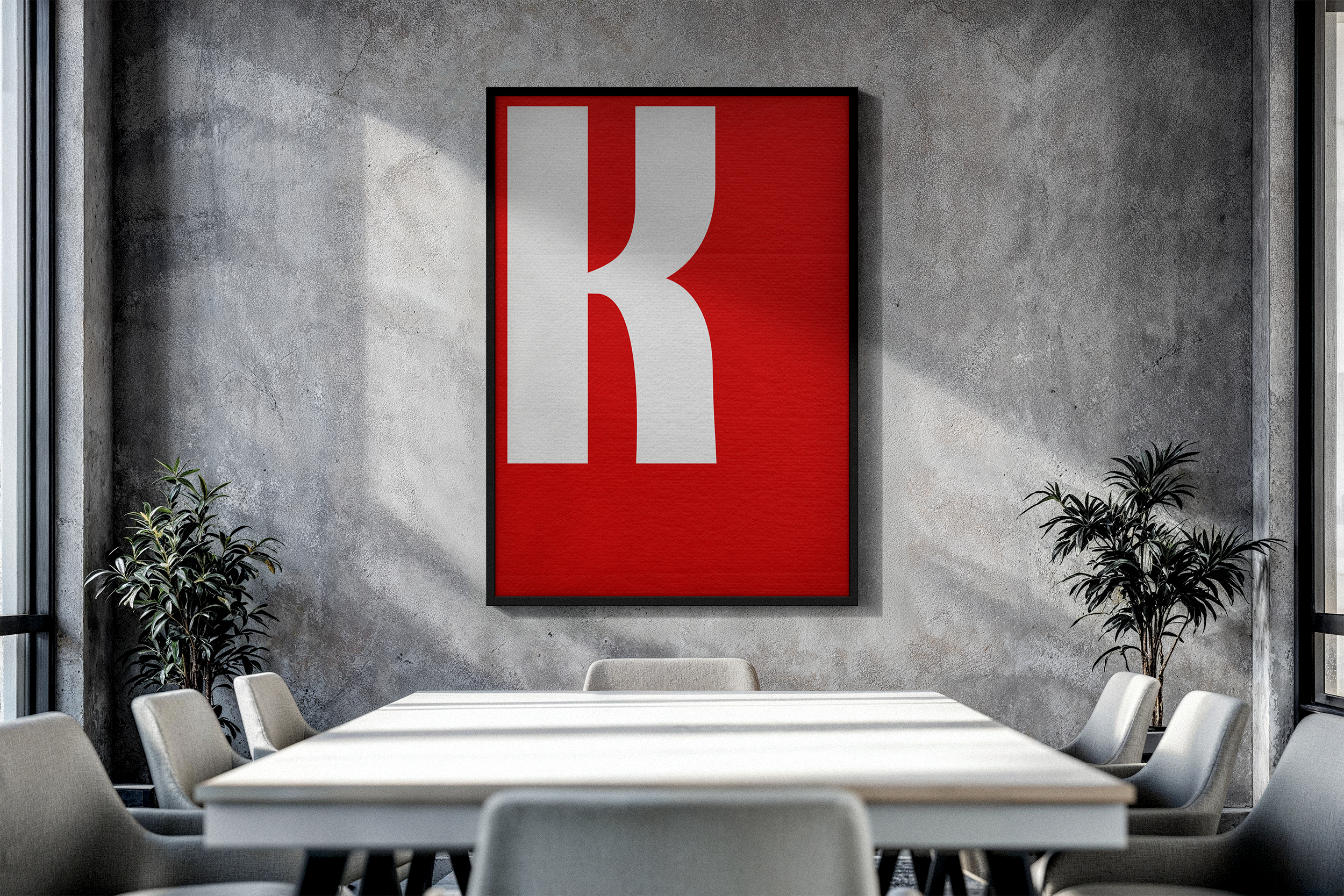A framed poster featuring a large, white, block letter 'K' on a vibrant red textured background, mounted on a raw concrete wall in a modern conference room.