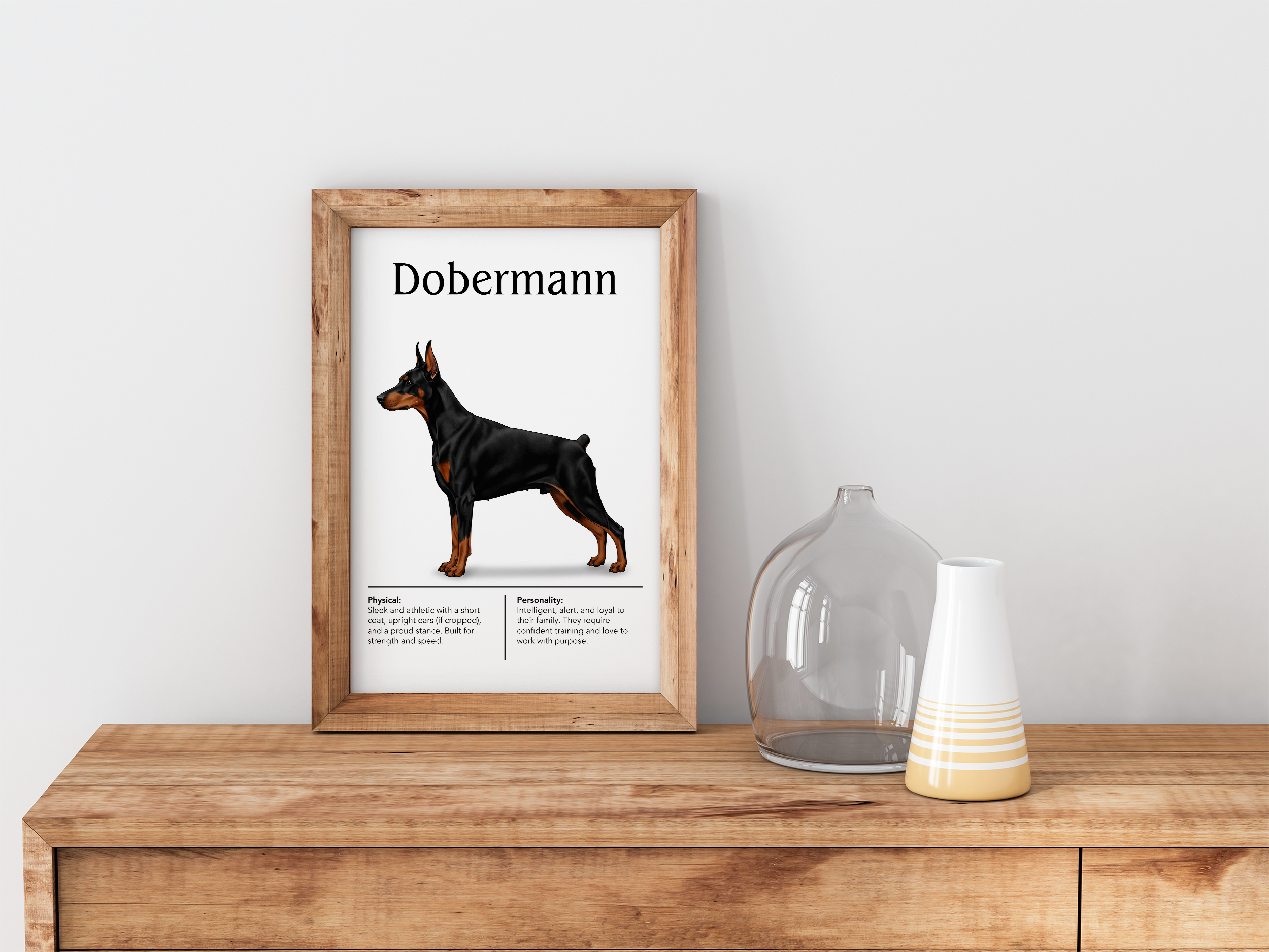 A wood-framed poster of a black and tan Dobermann, standing on a light wooden dresser next to a clear glass vase and a white and yellow decorated vase.