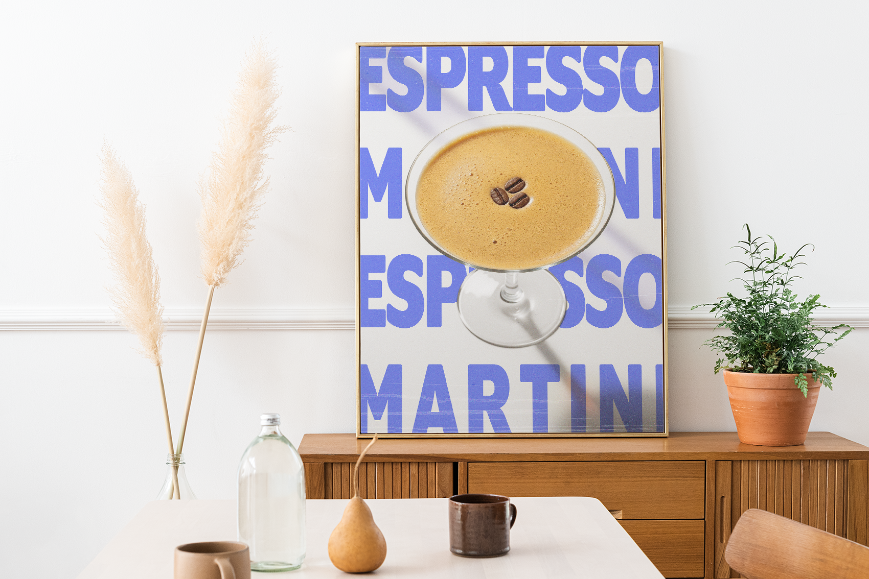 Framed poster of an Espresso Martini cocktail with three coffee beans, over a light blue background with repeating 'ESPRESSO MARTINI' text, placed on a wooden cabinet in a bright dining area.