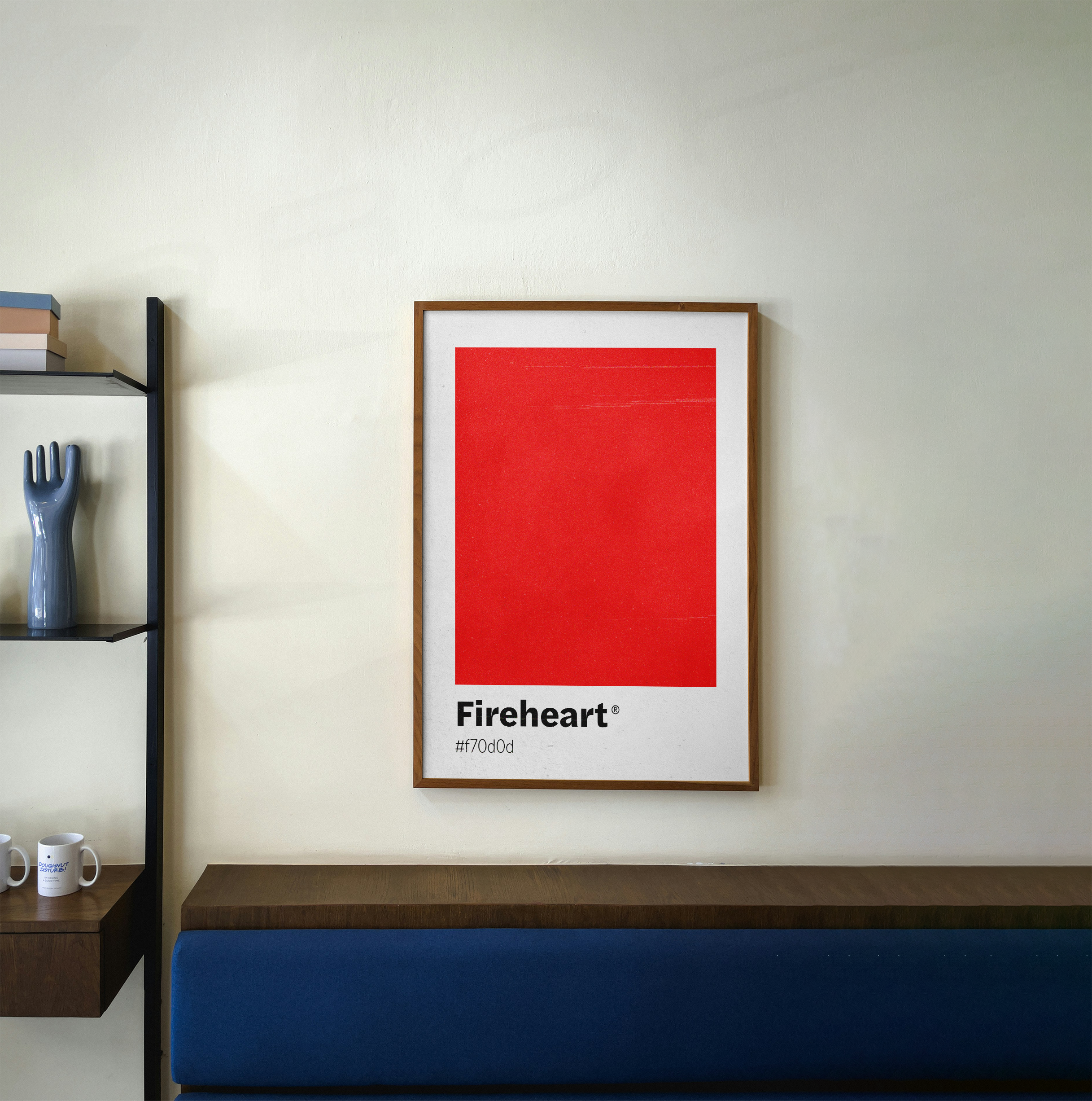 A wood-framed minimalist poster with a large, textured red square labeled "Fireheart" and its hex code, hanging above a blue cushioned bench in a kitchen or dining area.