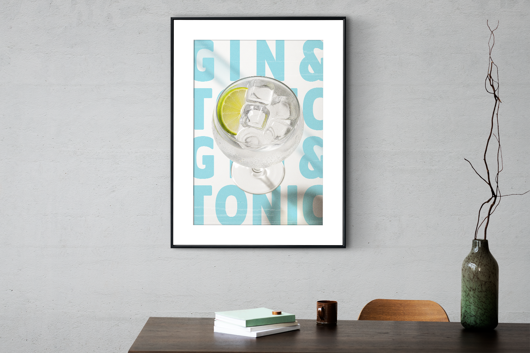 Black framed poster of a Gin & Tonic cocktail with a lime slice and ice, set against a repeating light blue and white background, hanging above a dark wooden table.
