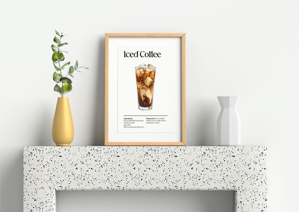 A clean, minimalist art print featuring a realistic illustration of a glass of iced coffee, complete with simple ingredients and preparation instructions listed below. Essential decor for a kitchen, coffee bar, or cafe. The framed print is centered on a speckled white terrazzo surface, flanked by a modern gold vase with eucalyptus and a white geometric vase, for a chic and bright display.