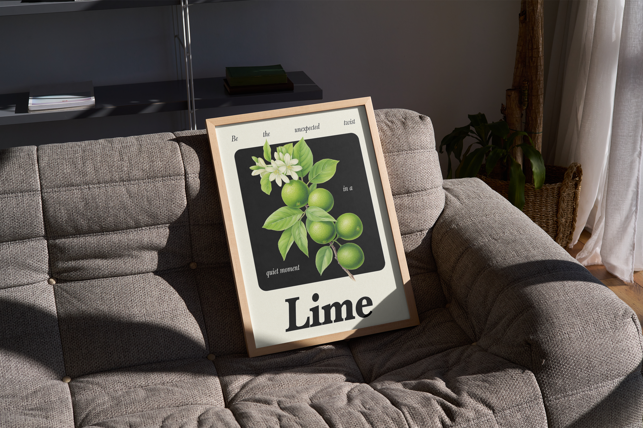 A wood-framed print featuring a botanical illustration of green limes and white blossoms on a branch against a dark background, with the word "Lime" and surrounding quote text, propped on a gray, textured sofa in a sunlit corner.