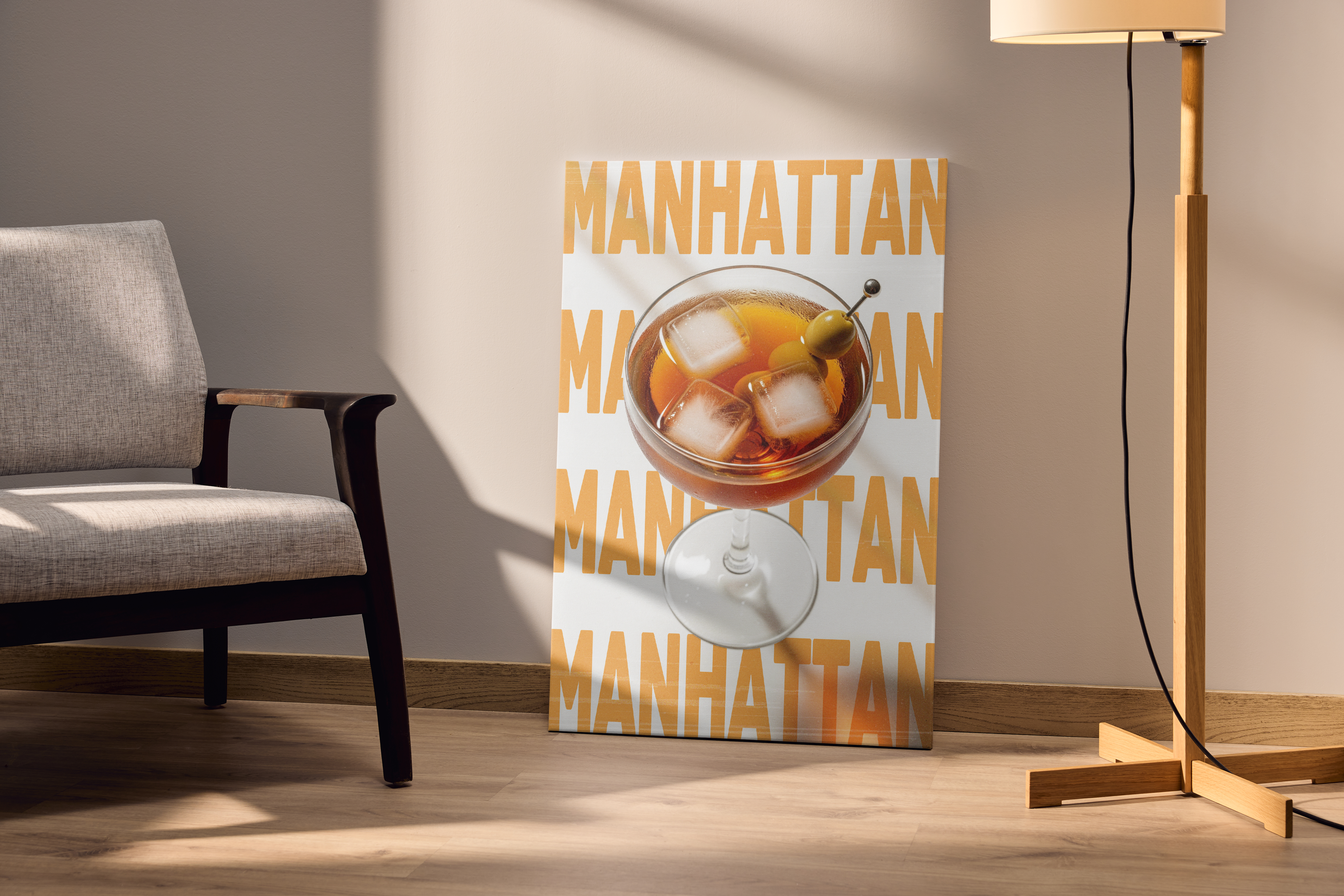 A large print of a Manhattan cocktail with repeating text on a white background, leaning on the floor next to a gray armchair and a wooden floor lamp.