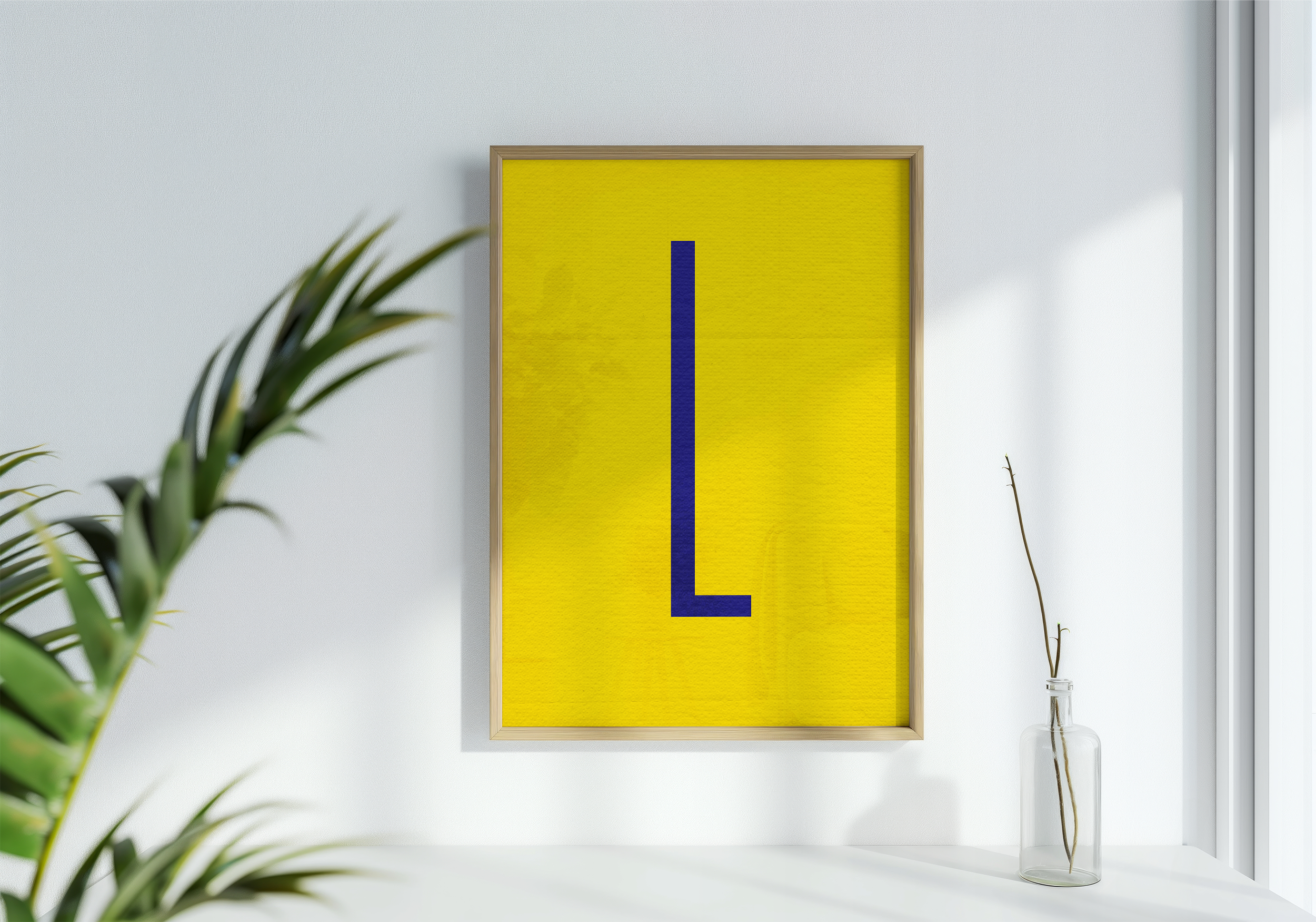 A framed poster with a thin, dark blue letter 'L' centered on a bright yellow background, displayed next to a leafy green houseplant in a bright, white room.