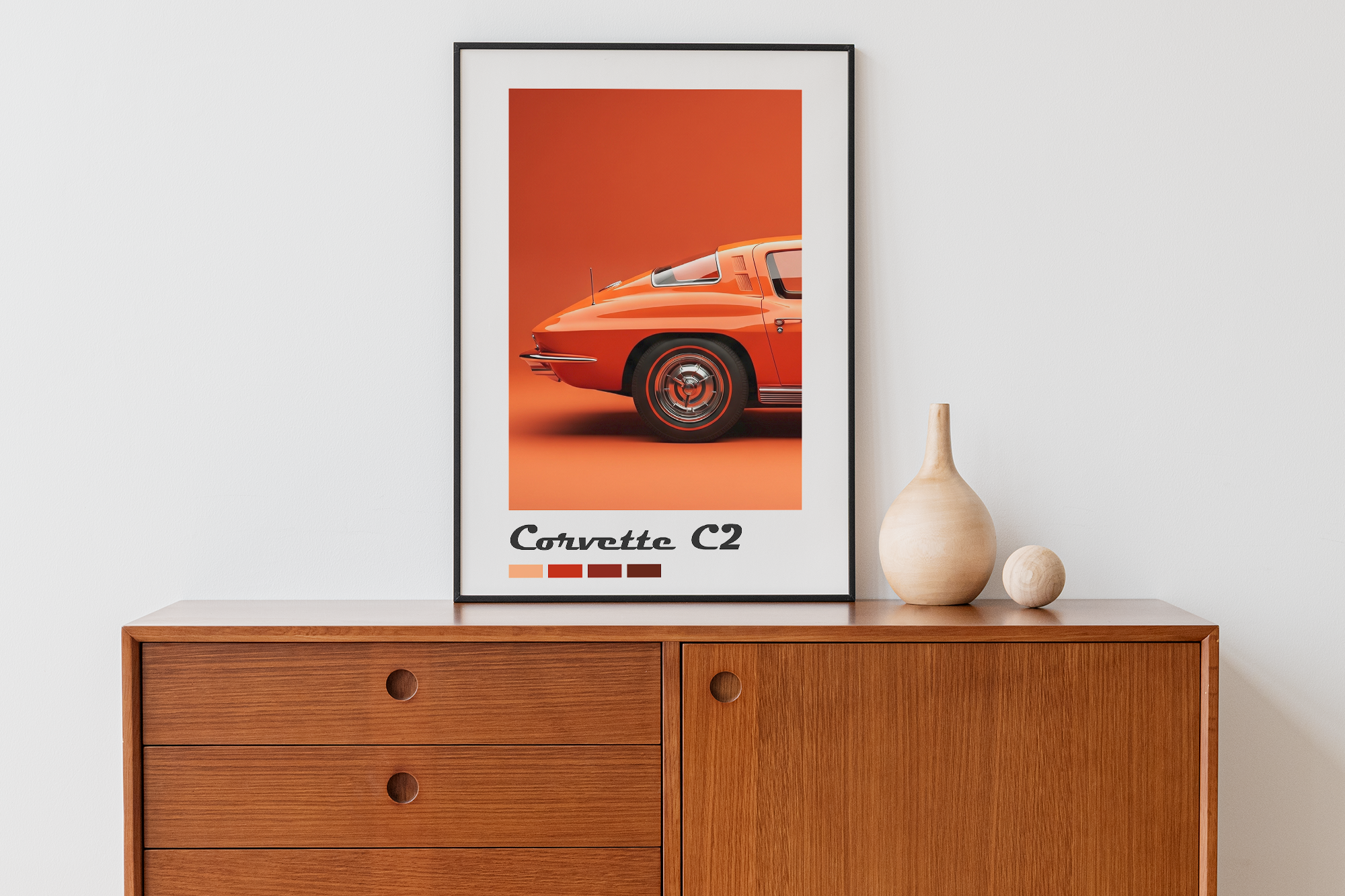 A black-framed print featuring a close-up rear view of a bright orange classic Corvette C2 sports car with color swatches below, resting on a mid-century modern wooden cabinet.