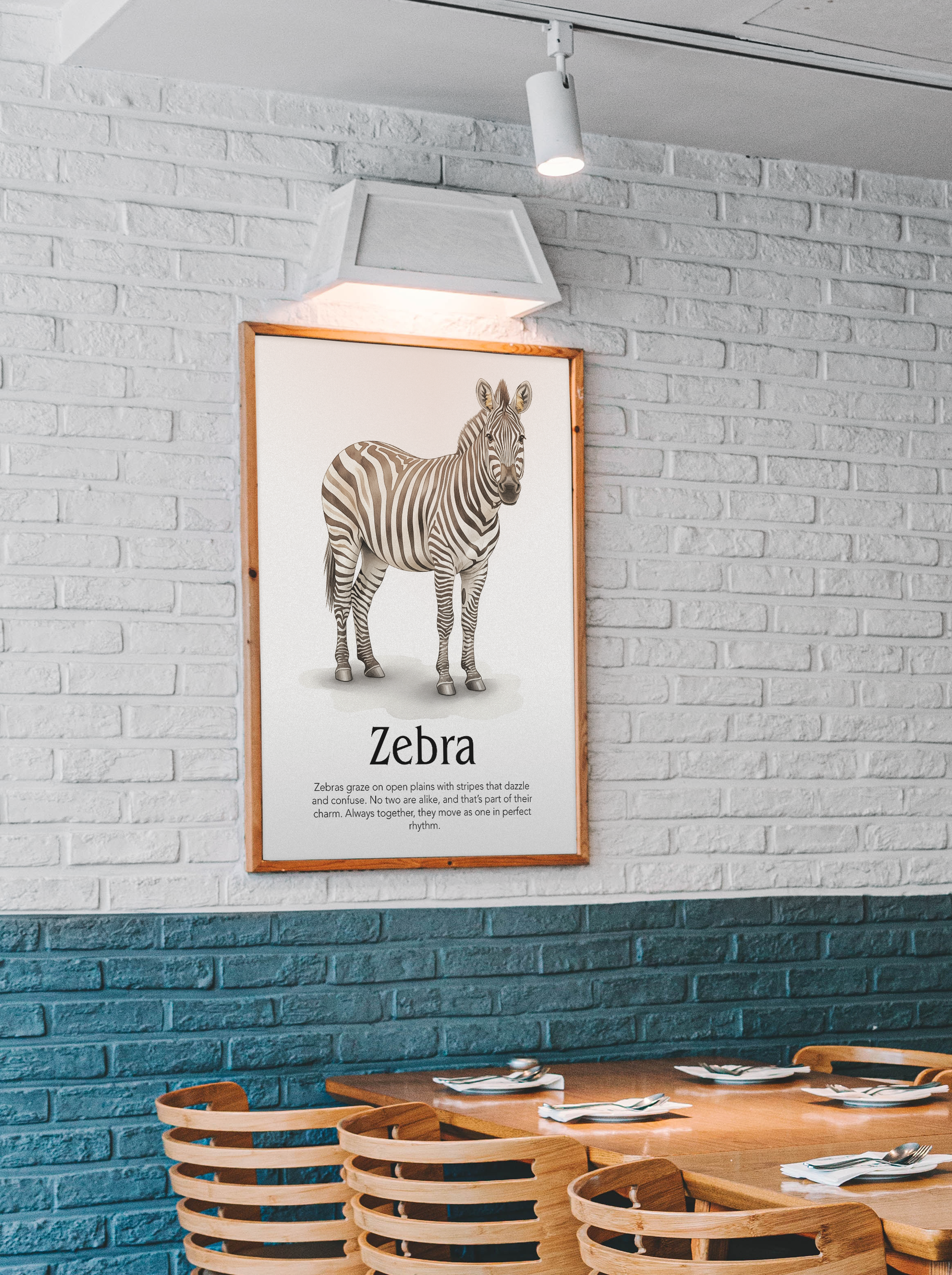 A striking animal art print featuring a detailed, realistic illustration of a zebra, along with a short text describing its herd behavior and distinct stripes. Ideal for a cafe, dining area, or a natural history-themed room. The wood-framed print is mounted on a textured white brick wall, illuminated by a track light, hanging above a wooden table with rattan-backed chairs.