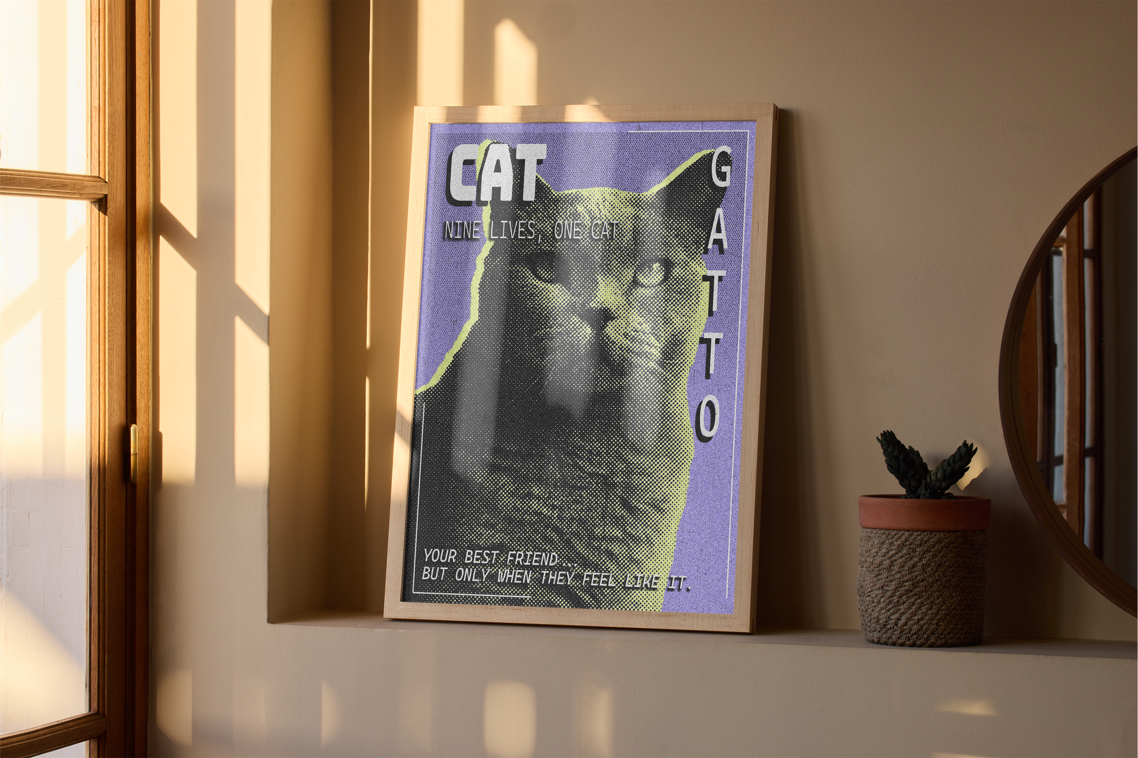A wood-framed poster with a retro, grainy image of a Cat and the words "CAT GATTO" and "NINE LIVES, ONE CAT," resting on a bathroom shelf next to a small mirror and a potted plant.