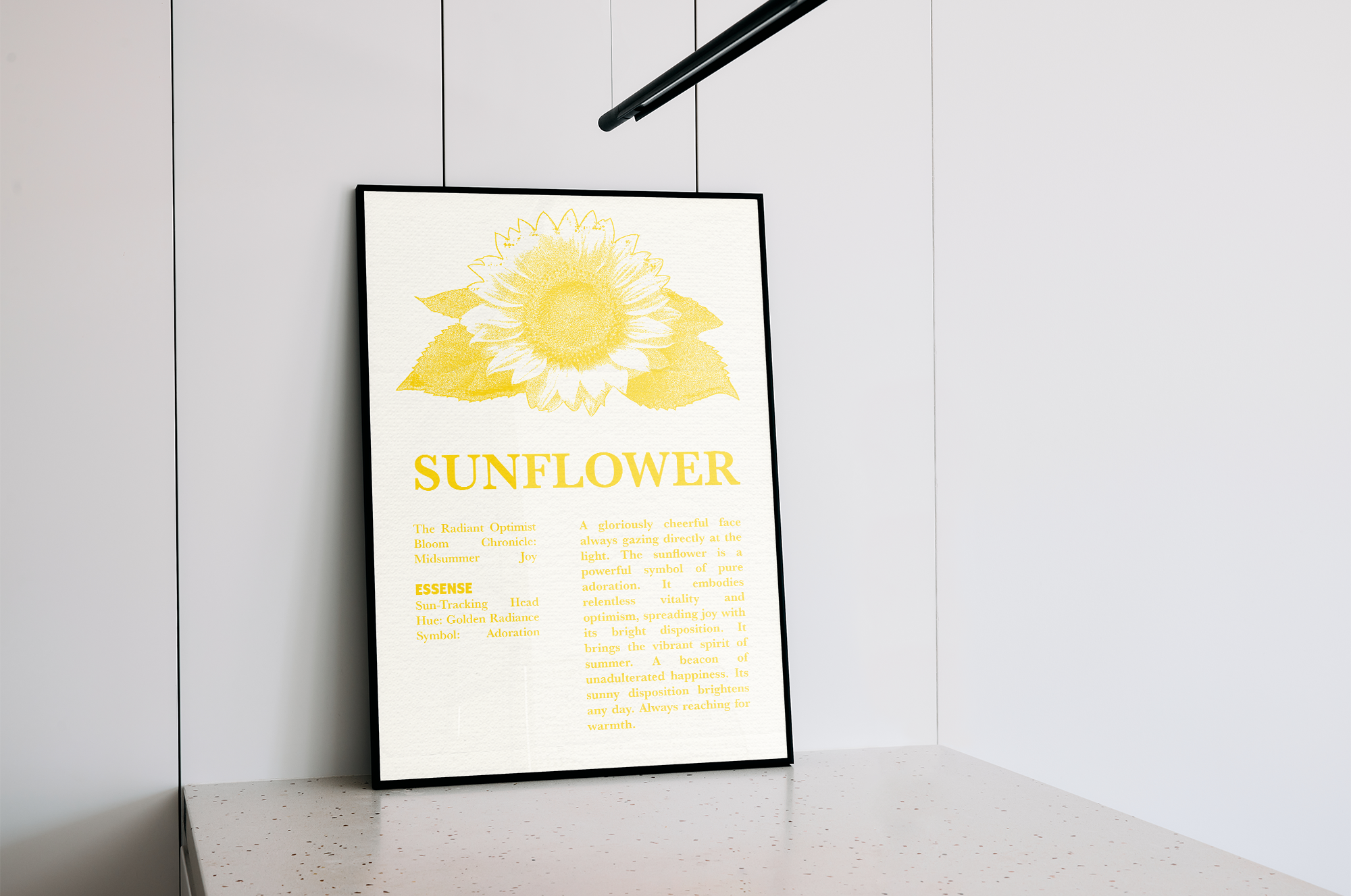 A black-framed poster featuring a yellow, stipple-style illustration of a sunflower with the title "SUNFLOWER" and detailed descriptions of its meaning and attributes, leaning on a speckled white kitchen counter under a modern pendant light.